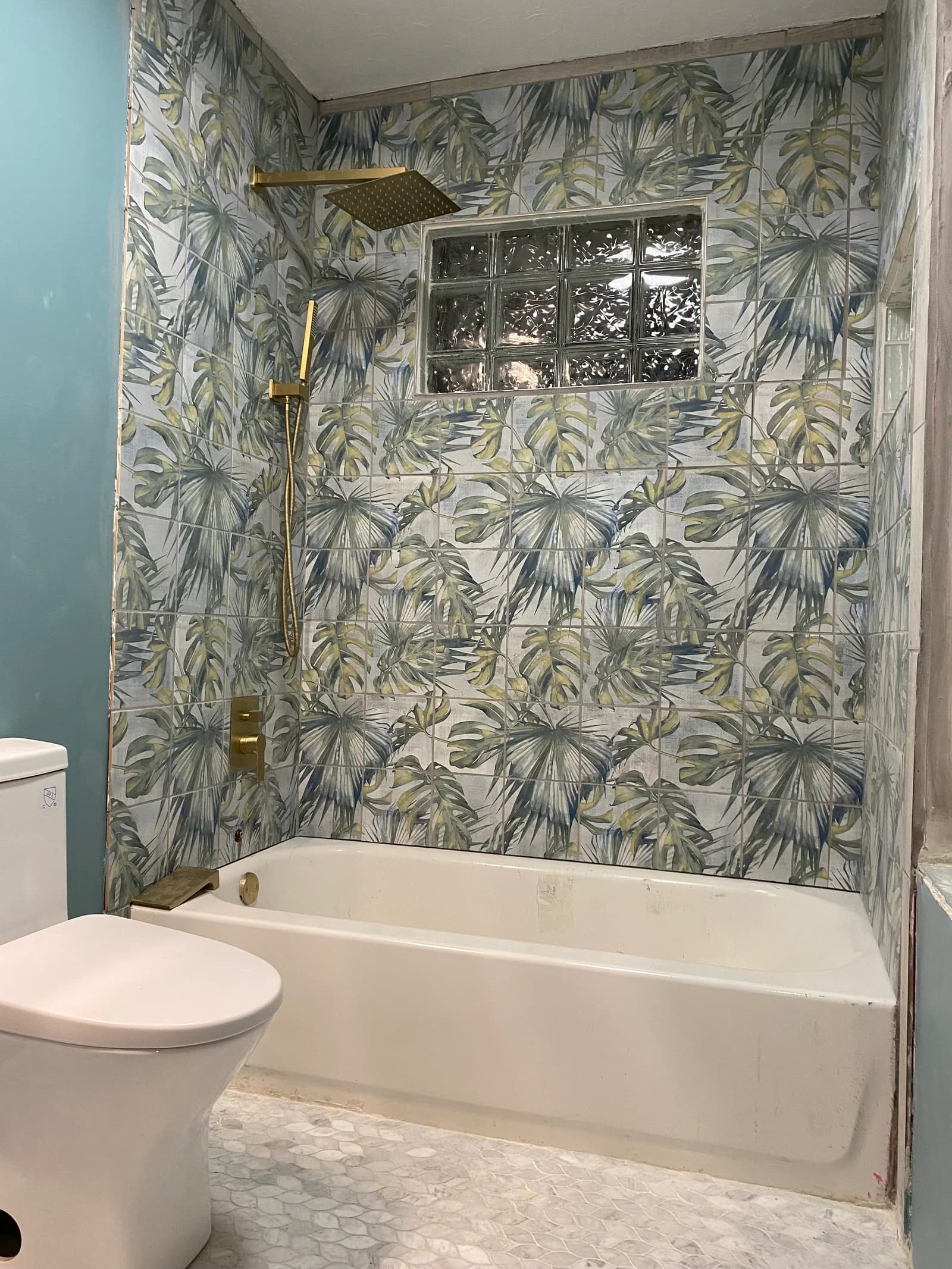 Bathtub and shower with botanical walls, a glass-block window, and brass fixtures