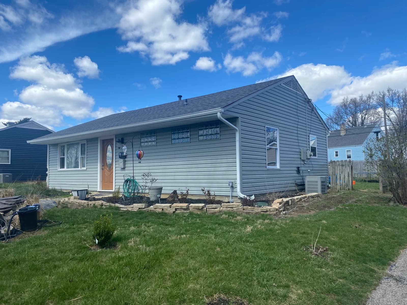 Front and side view of the house with gray siding and a wooden front door