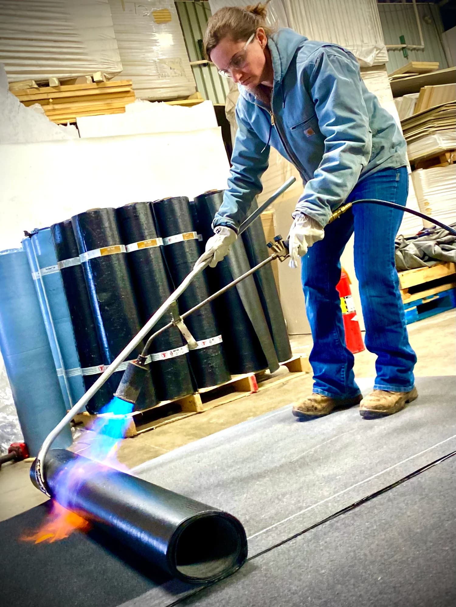 Tillie wearing safety glasses and gloves while working with a torch on rolled roofing material