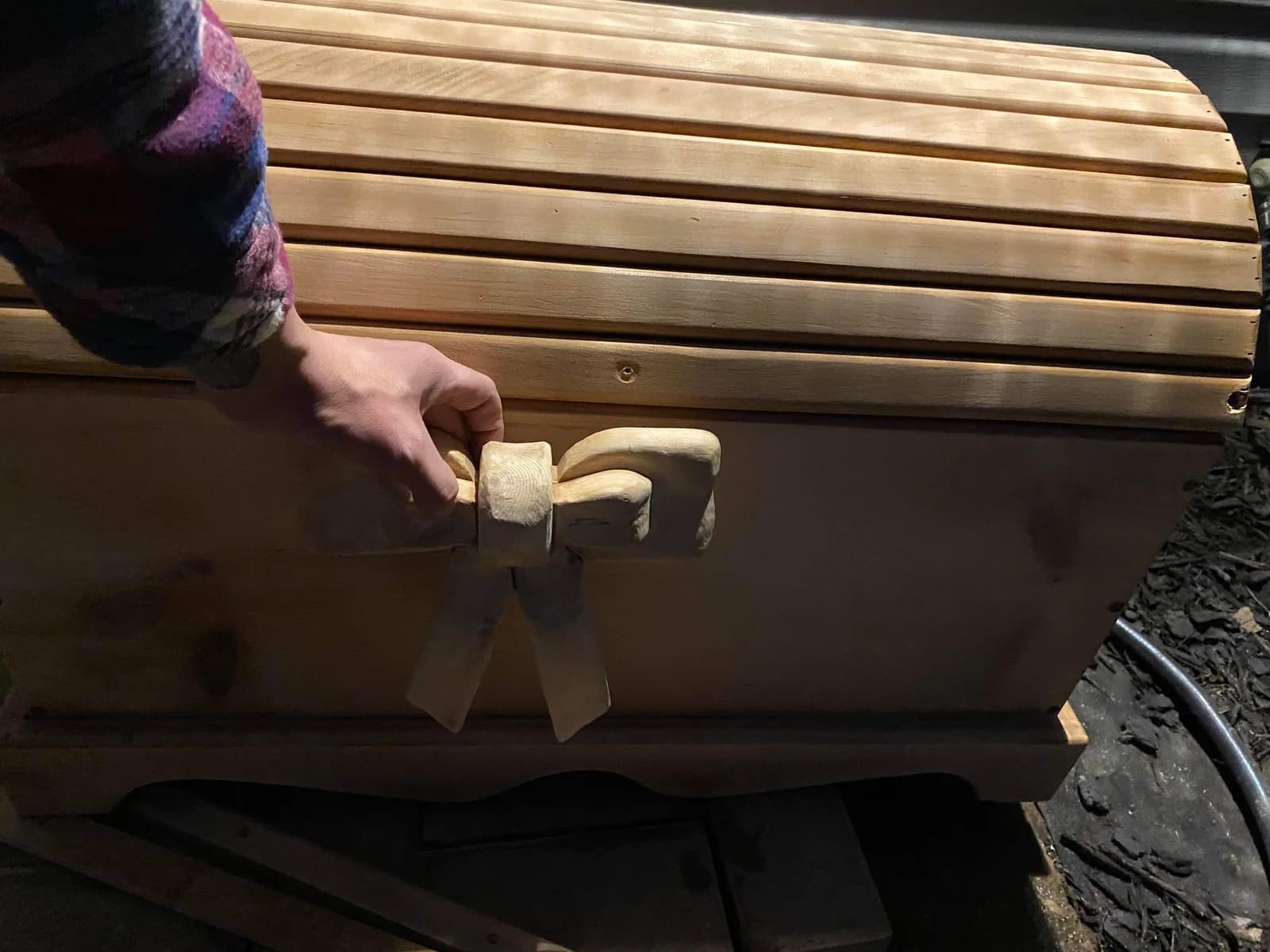 Wooden chest with a curved slatted lid and a carved bow held against the front